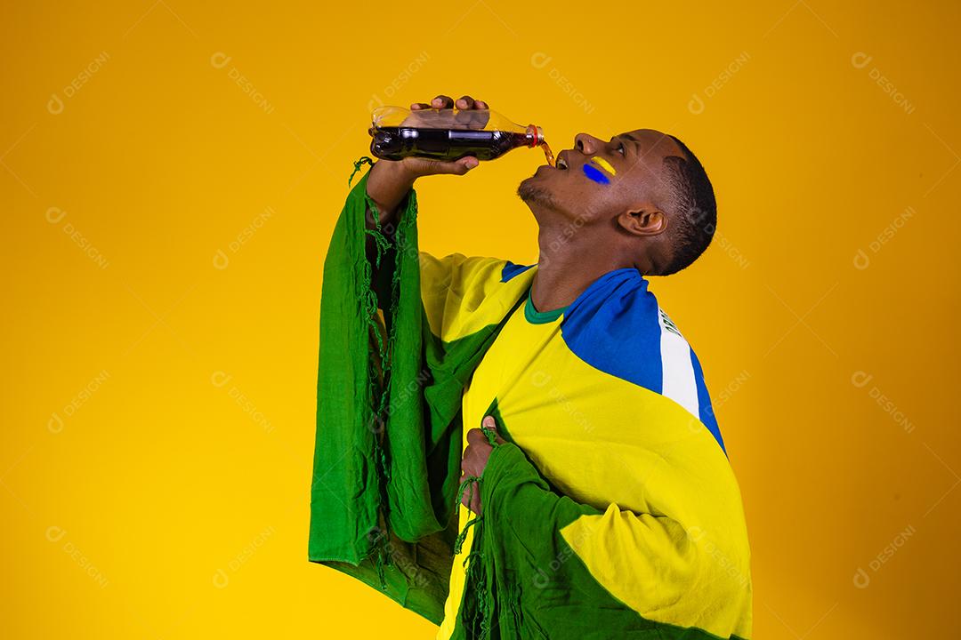 Homem afro, fã brasileiro, bebendo um líquido preto de uma garrafa. homem fã brasileiro com refrigerante de cola