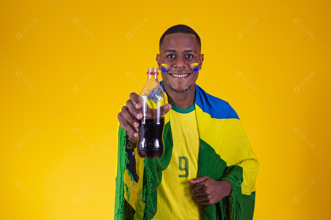 Homem afro, fã brasileiro, bebendo um líquido preto de uma garrafa. homem fã brasileiro com refrigerante de cola