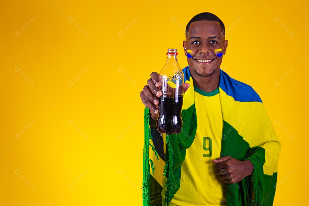 Homem afro, fã brasileiro, bebendo um líquido preto de uma garrafa. homem fã brasileiro com refrigerante de cola