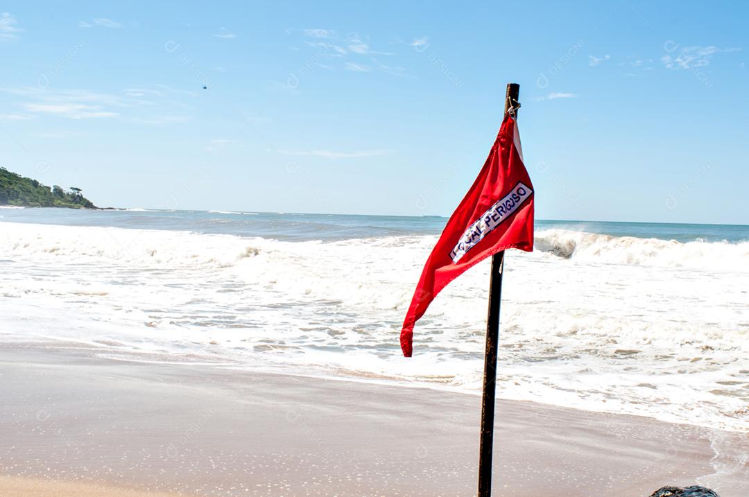 Praia em dia ensolarado com bandeira vermelha escrita (lugar perigoso)