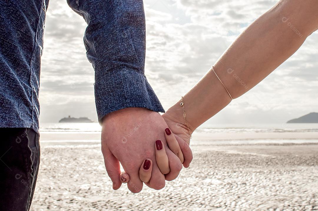 Casal apaixonado de mãos dadas na praia.