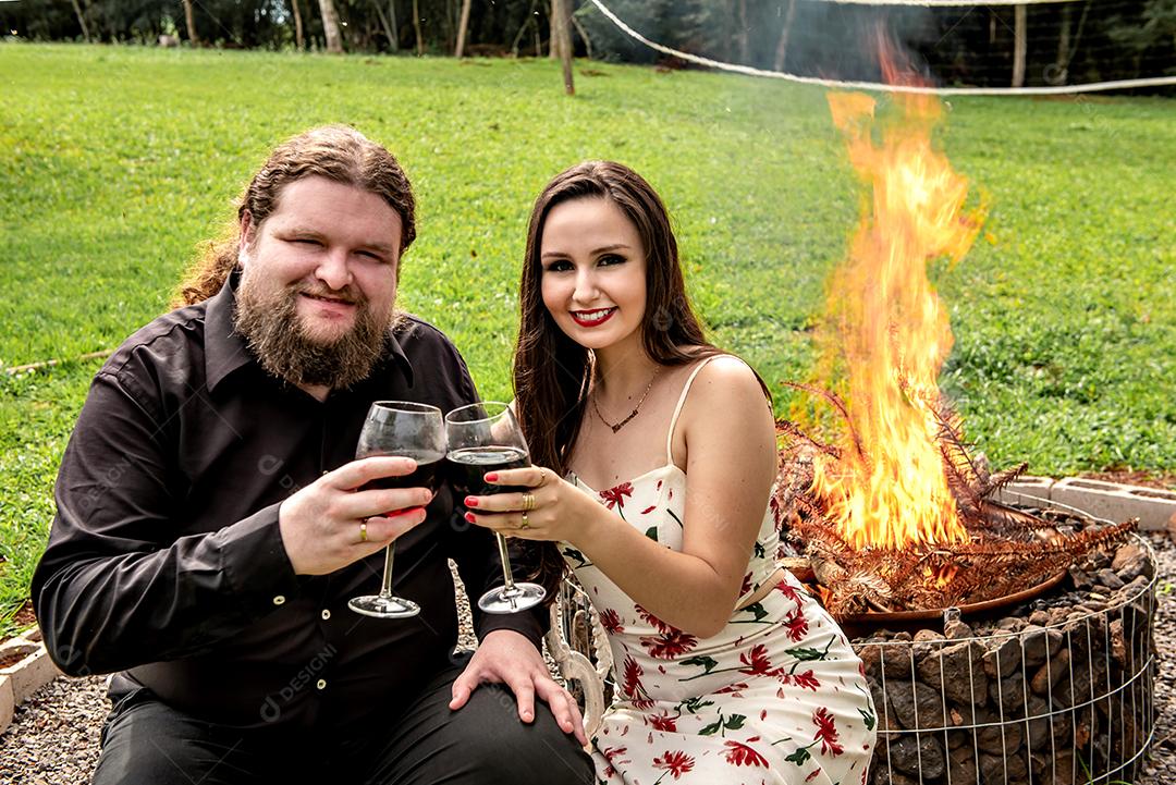 Casal apaixonado bebendo vinho em frente a uma fogueira no jardim