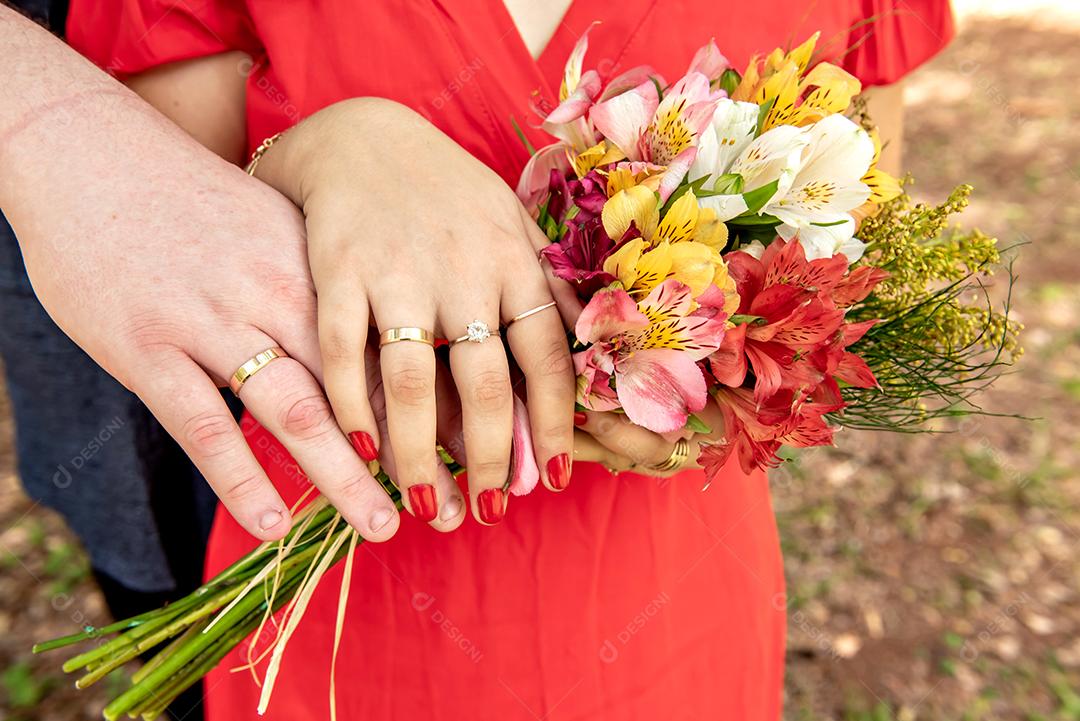 Mãos do casal segurando um buquê de flores.