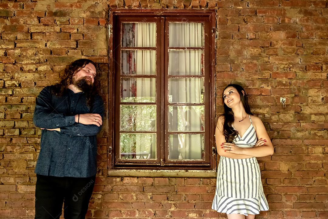 Casal de noivos relaxando na parede de tijolos e janela.