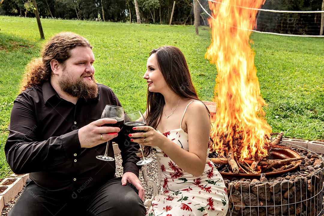 Amantes bebendo vinho em frente a uma fogueira no jardim