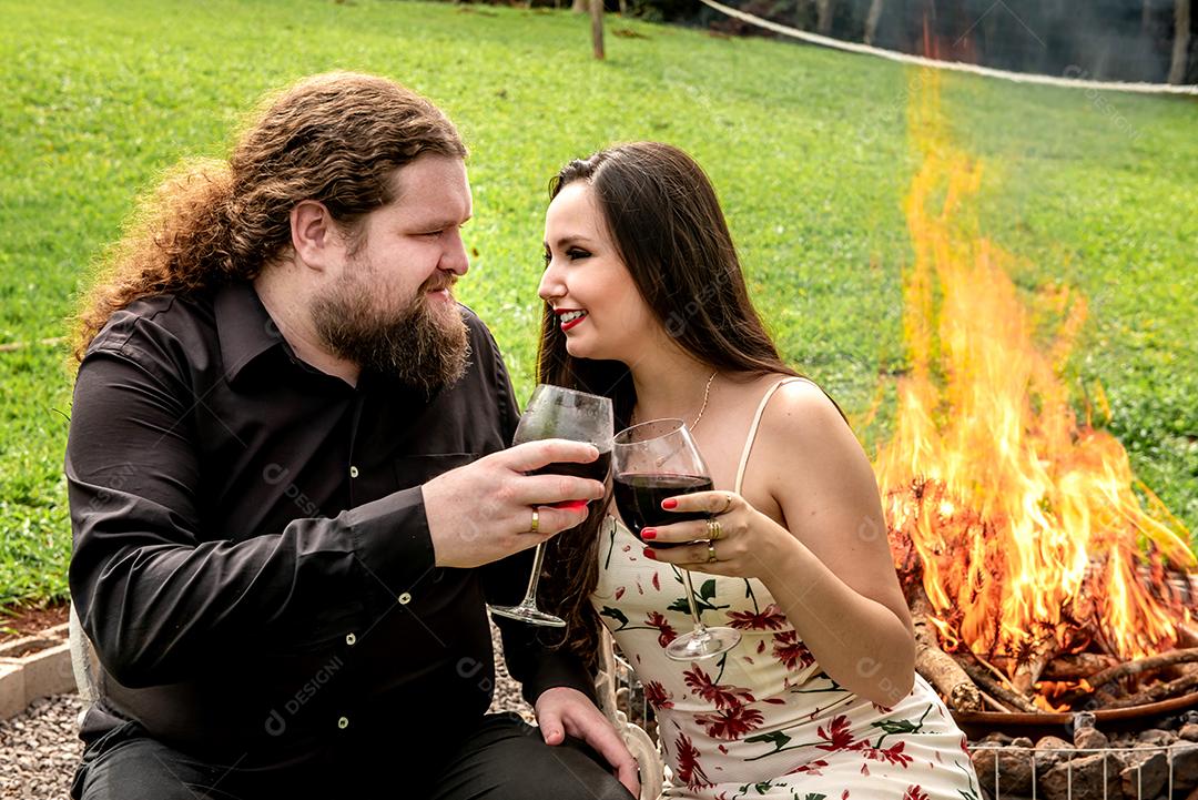 Amantes bebendo vinho em frente a uma fogueira no jardim