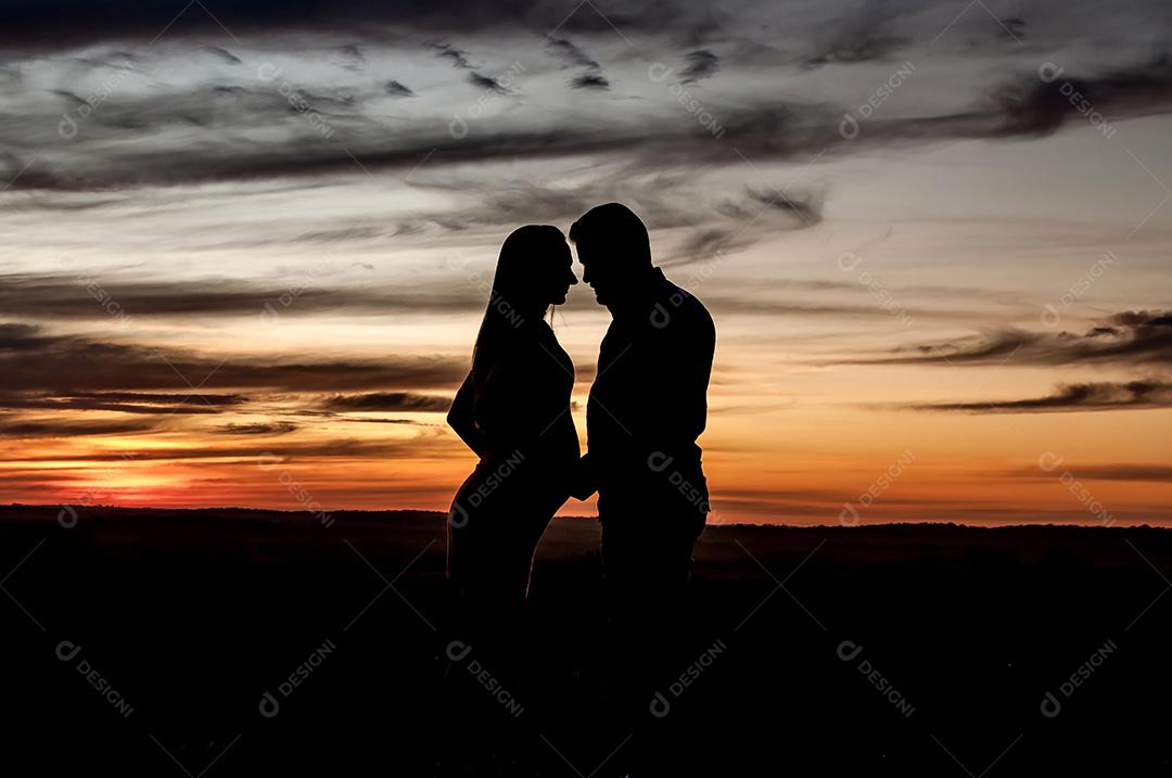 Silhouette of pregnant couple in love at orange sunset.