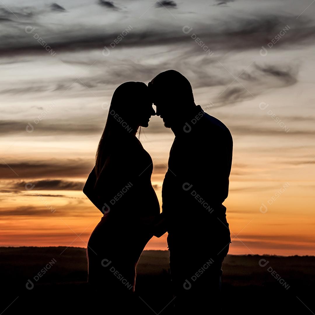 Silhueta de casal grávido apaixonado ao pôr do sol