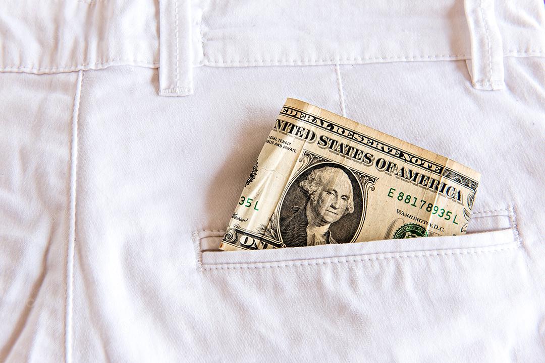 Uma nota de dólar dobrada no bolso da calça jeans branca.