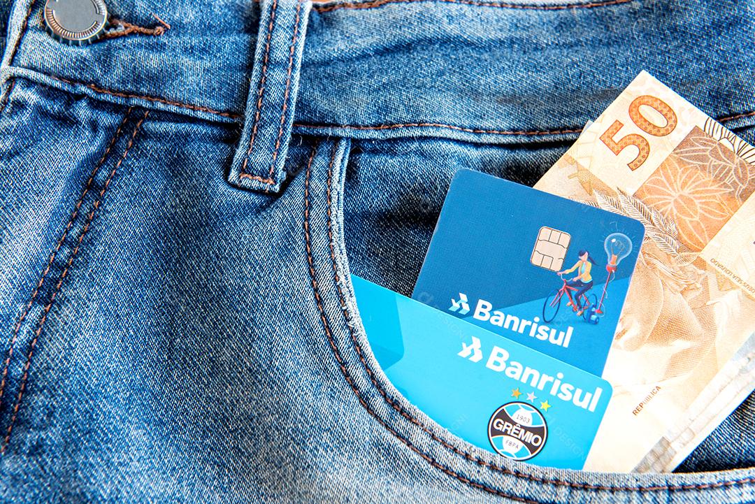 Cartões de crédito bancários brasileiros (banrisul) e dinheiro no bolso da calça jeans.