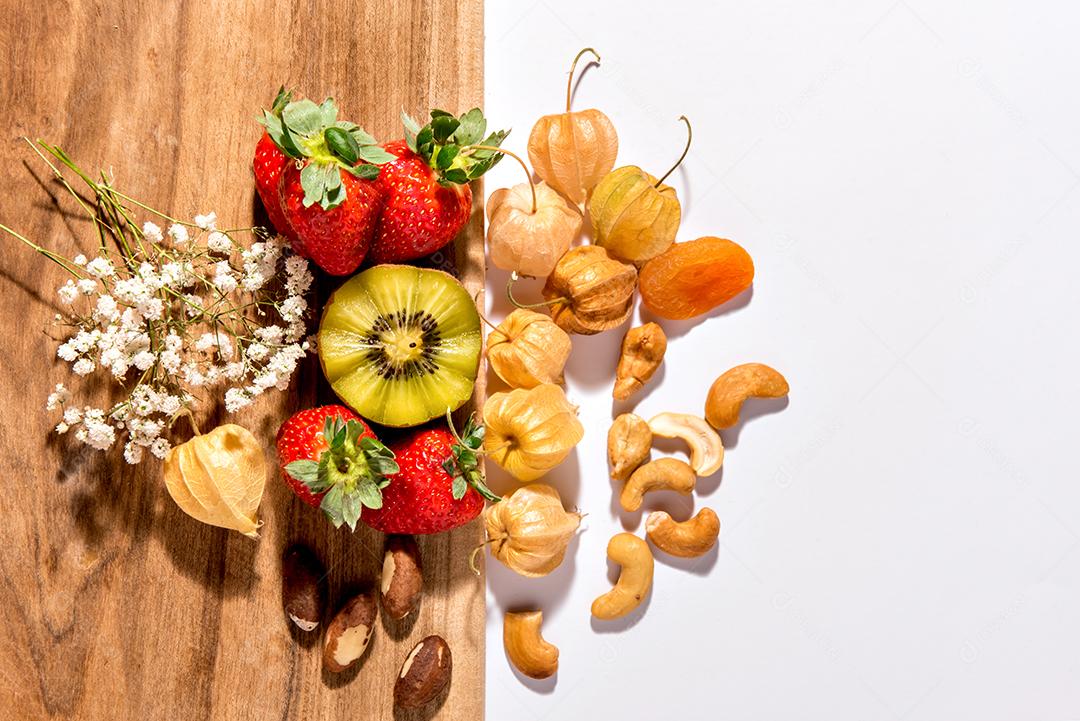 Kiwi, morangos, castanha de caju, castanha do Brasil e physalis em fundo de  madeira