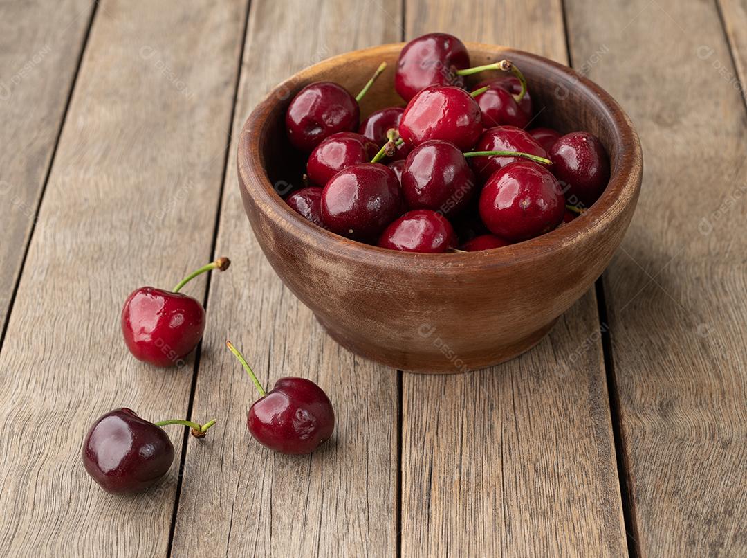 Cerejas vermelhas em uma tigela sobre a mesa de madeira