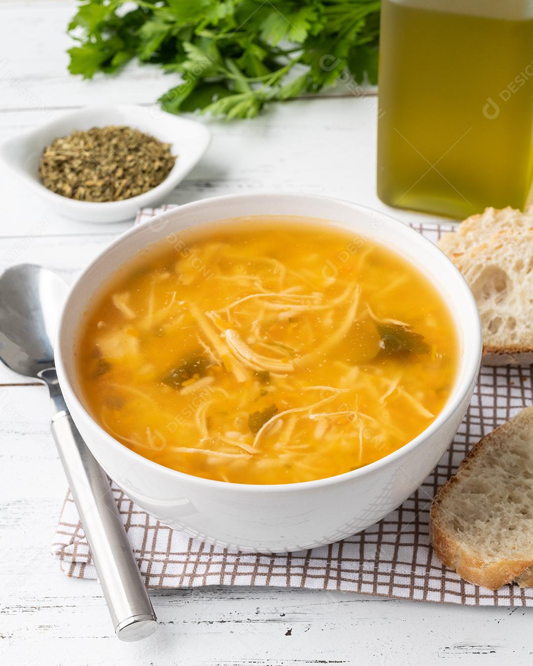Sopa de galinha em uma tigela com fatias de pão e tempero sobre madeira