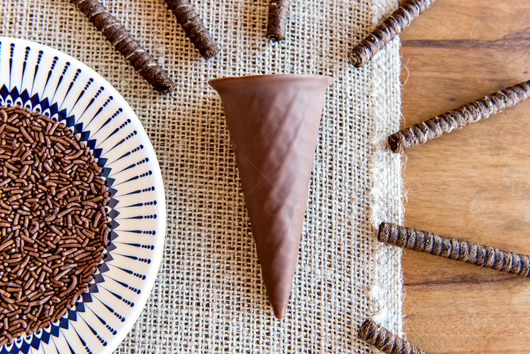 Casquinha de chocolate e canudos de chocolate e prato de chocolate granulado.