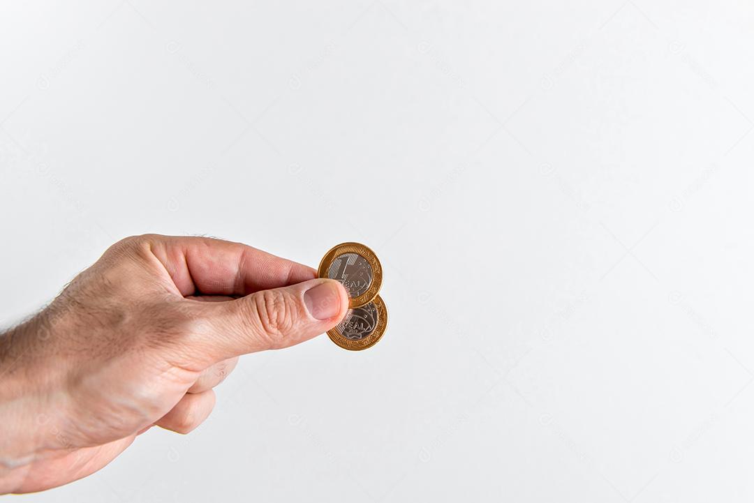 Mão segurando duas moedas de 1 real brasileiro, moedas reais brasileiras.
