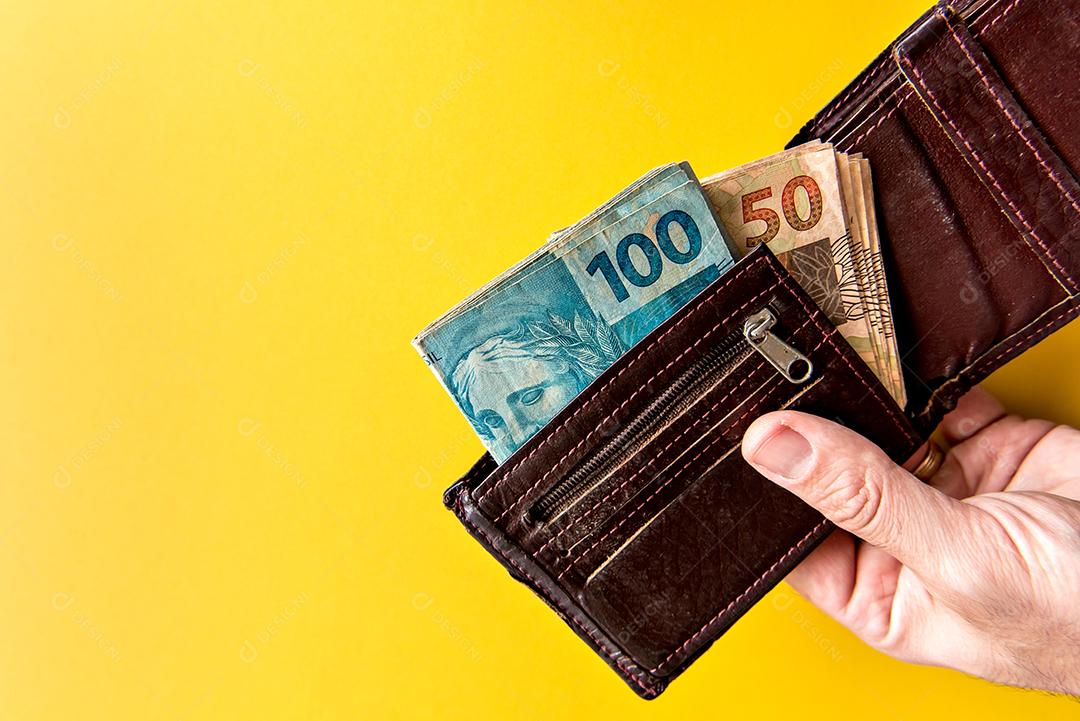 Mão segurando a carteira com dinheiro brasileiro, notas reais brasileiras