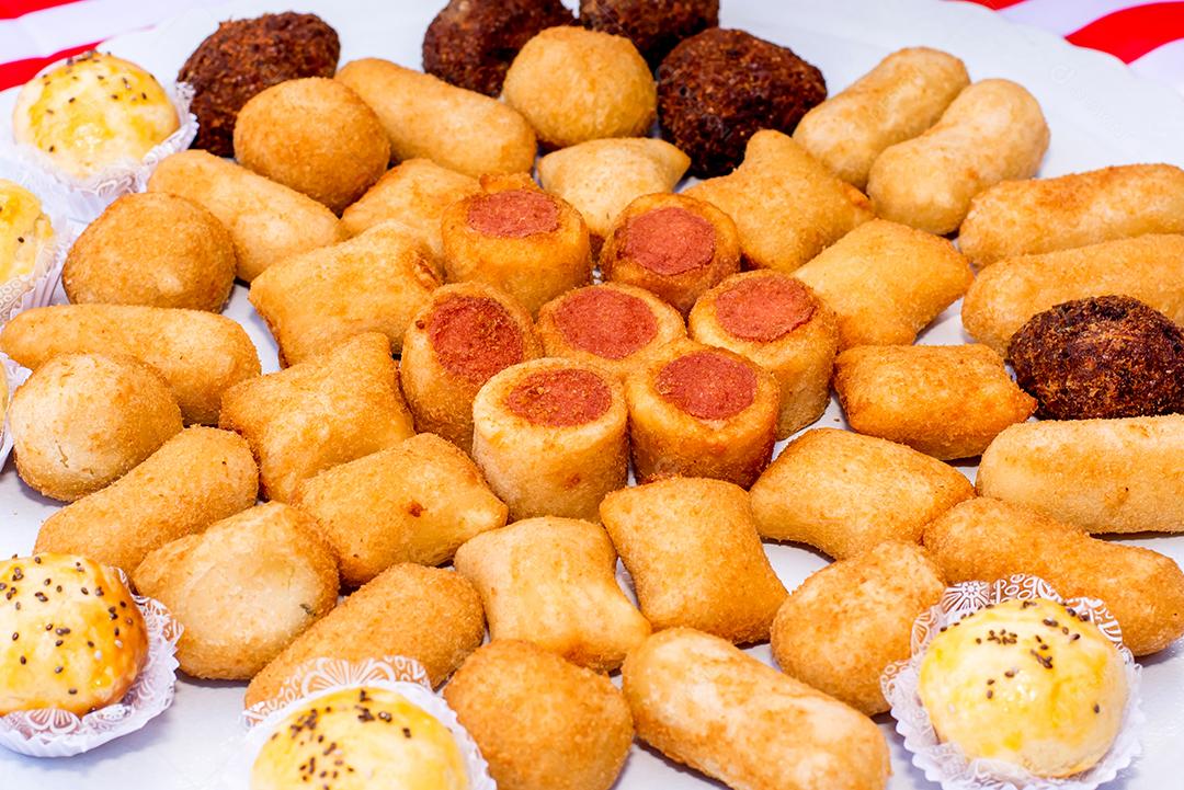 Mesa com bandeja de salgadinhos, pastéis, risolis e rolinhos de salsicha.