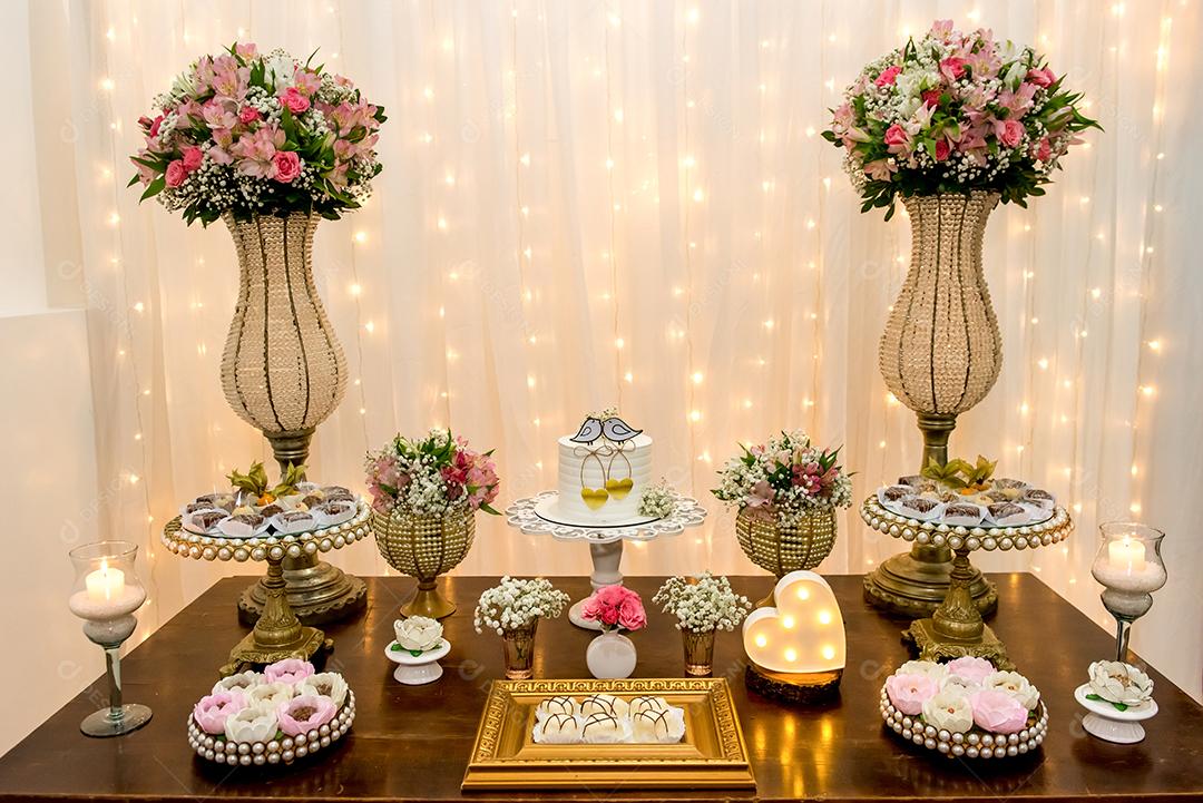 Mesa decorada com bolo, doces, velas, flores e enfeites
