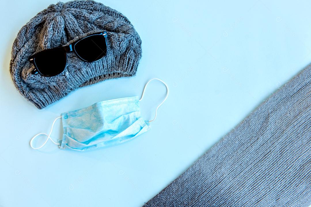Boné, óculos, máscara e cachecol sobre fundo azul