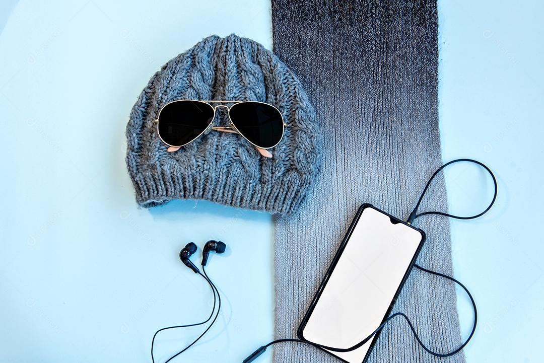 Boné, óculos de sol, cachecol e fones de ouvido sobre fundo azul