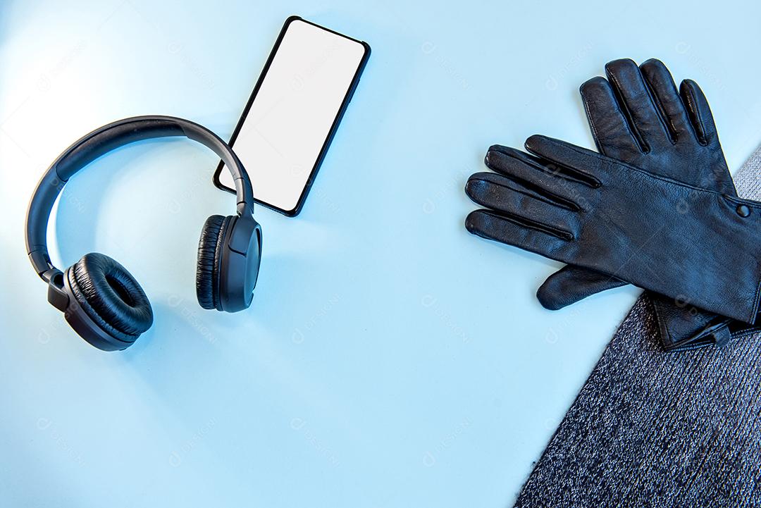 Fones de ouvido, celular, luvas e cachecol sobre fundo azul