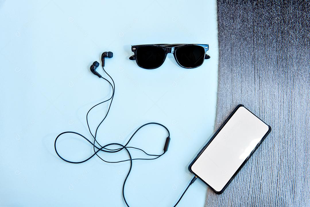 Fones de ouvido e smarthphone em fundo azul. Vista do topo.