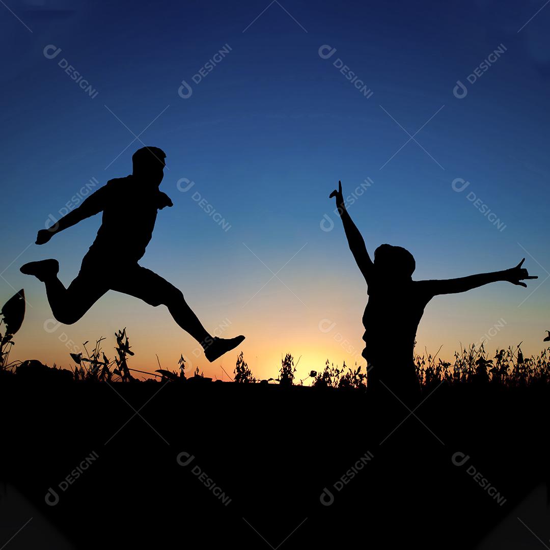 Silhueta de casal pulando no campo ao pôr do sol.