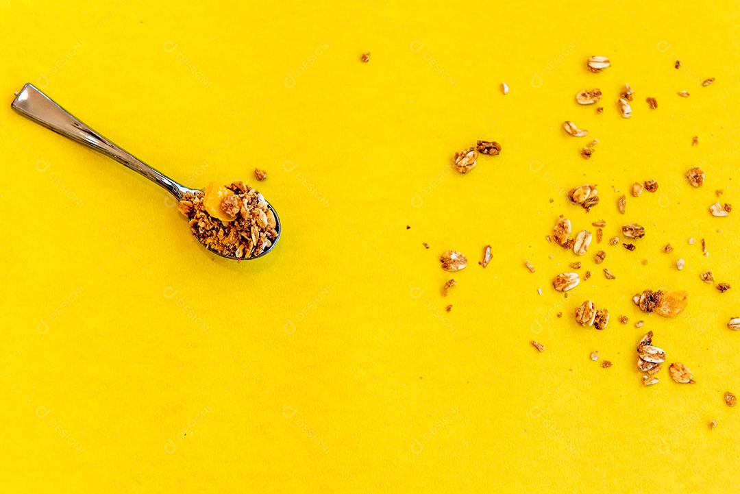 Colher com granola em fundo amarelo. Vista do topo.