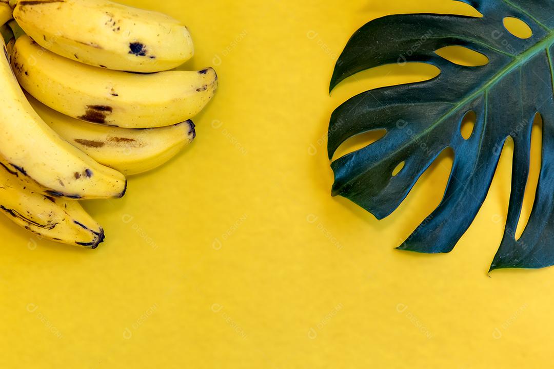 Bananas e folhagem de Rieb de Adão em fundo amarelo. Vista do topo.