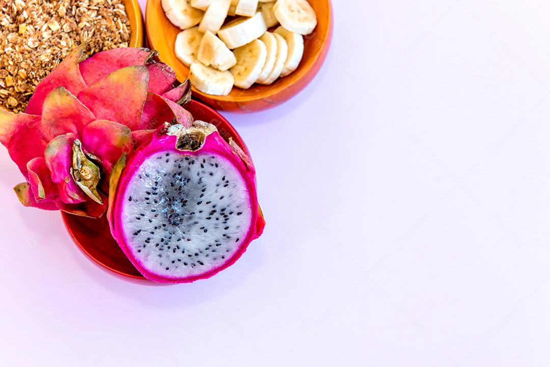 Prato com bananas fatiadas, granola e pitaya cortadas ao meio.