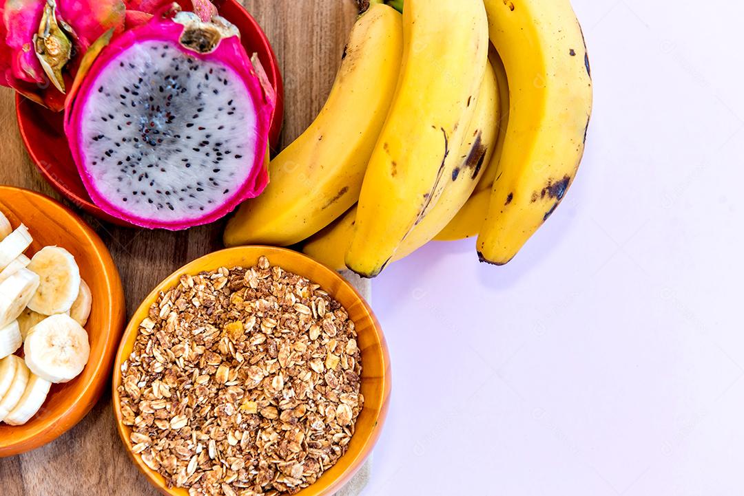 Prato com bananas fatiadas, granola e pitaya cortadas ao meio.