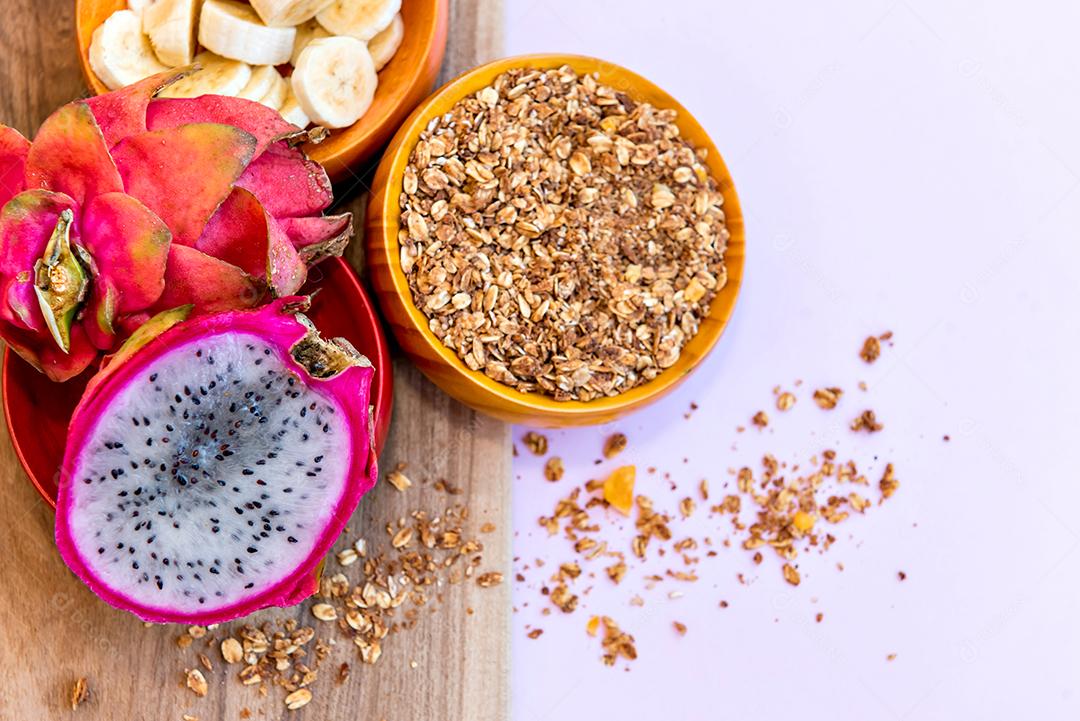 Prato com bananas fatiadas, granola e pitaya cortadas ao meio.