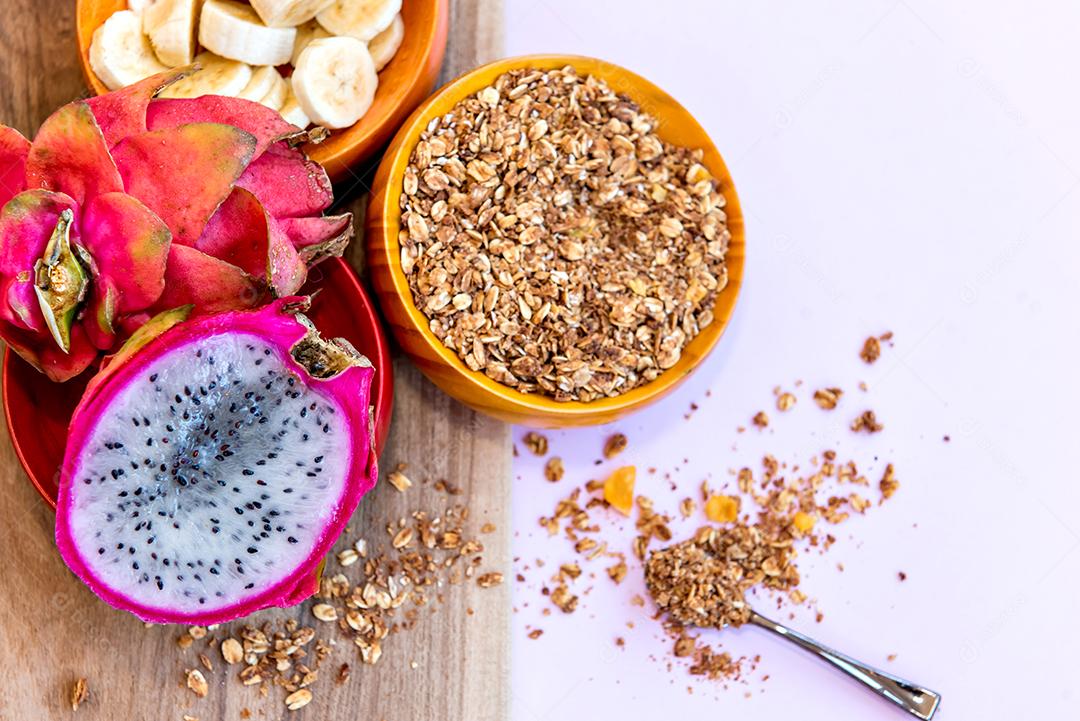 Prato com bananas fatiadas, granola e pitaya cortadas ao meio.