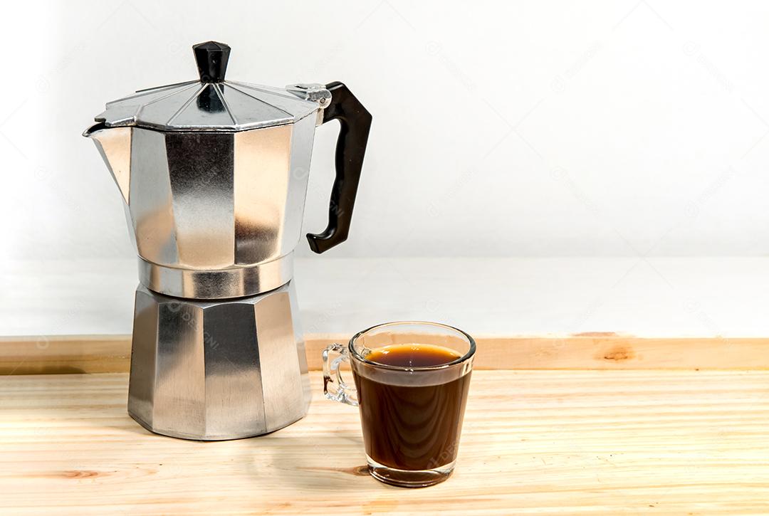Cafeteira italiana com café expresso na mesa de madeira branca.