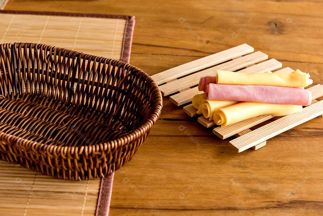 Ham and cheese with empty bread basket on breakfast table.