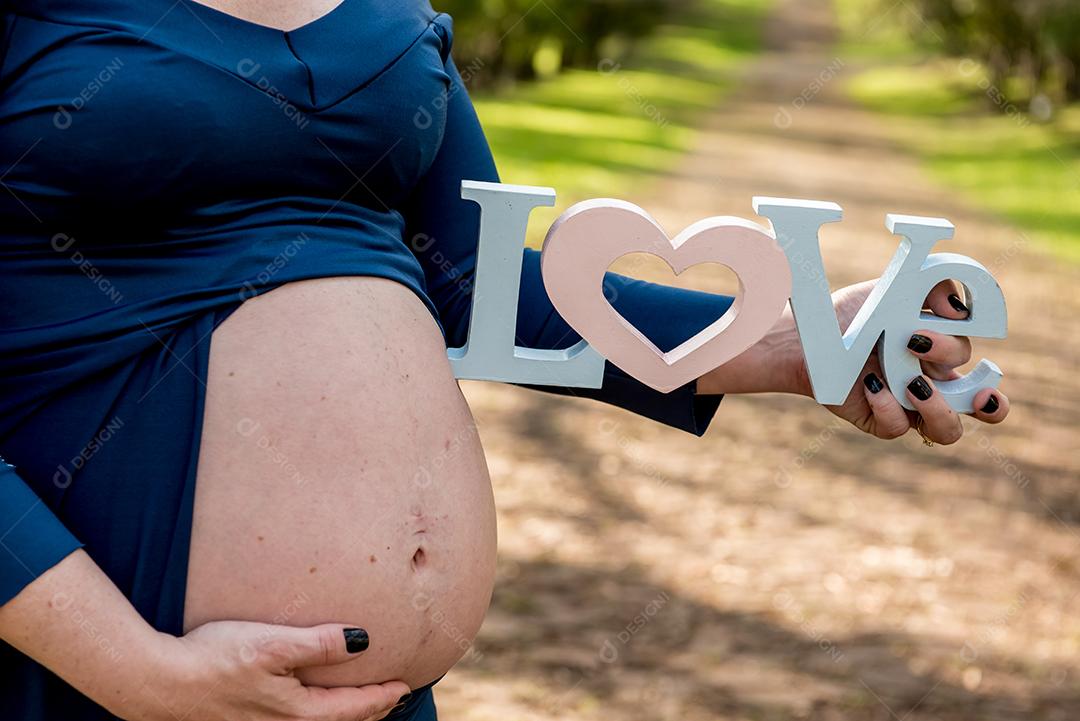 Mulher grávida mostrando a barriga e segurando sinal escrito amor.