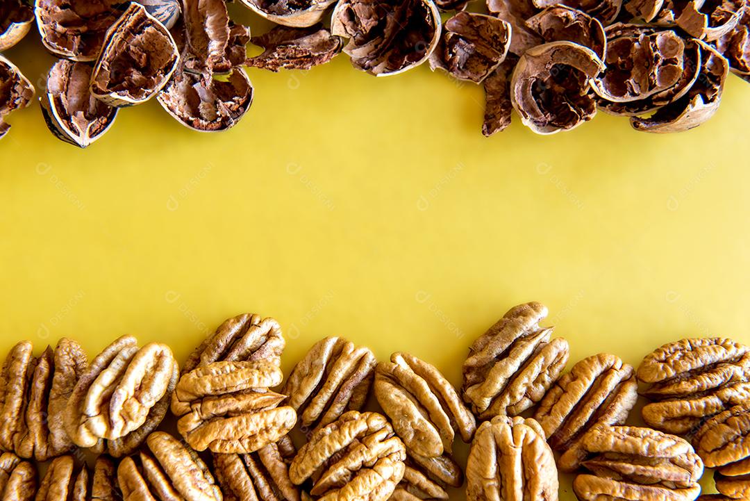 Nozes pecan descascadas em fundo amarelo.