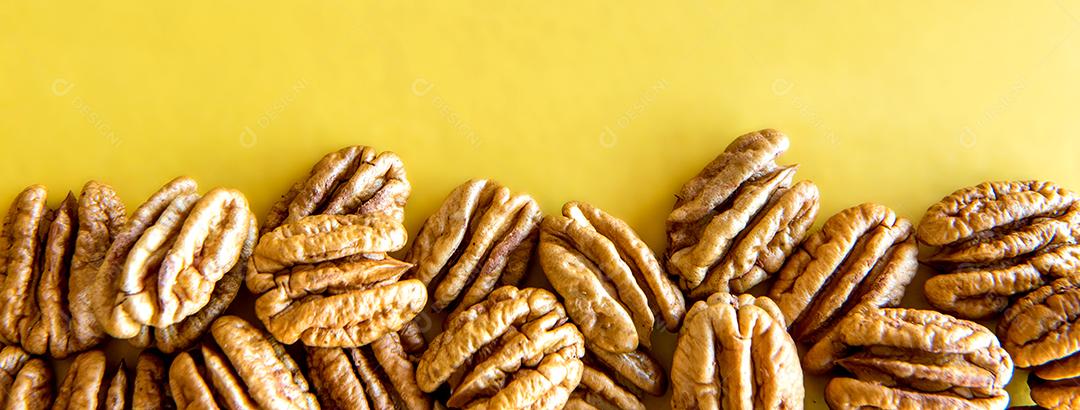 Nozes pecan descascadas em fundo amarelo.