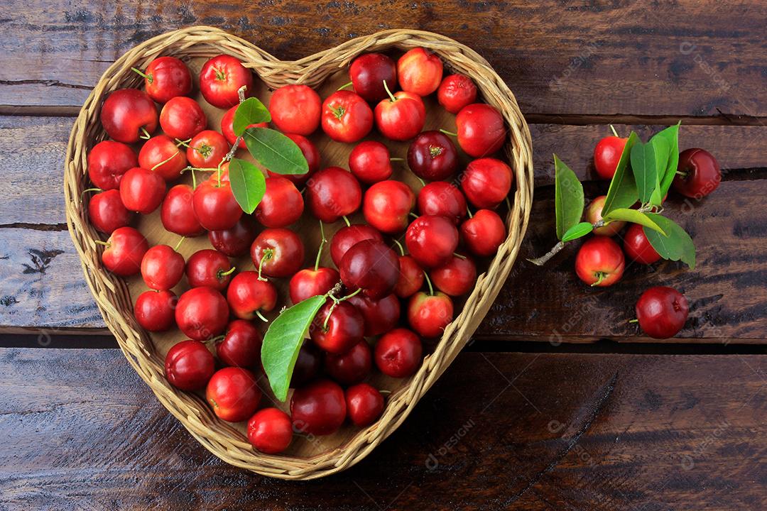 Acerola cereja crua, fresca, na cesta com forma de coração na mesa de madeira rústica, frutas antioxidantes. Vista do topo