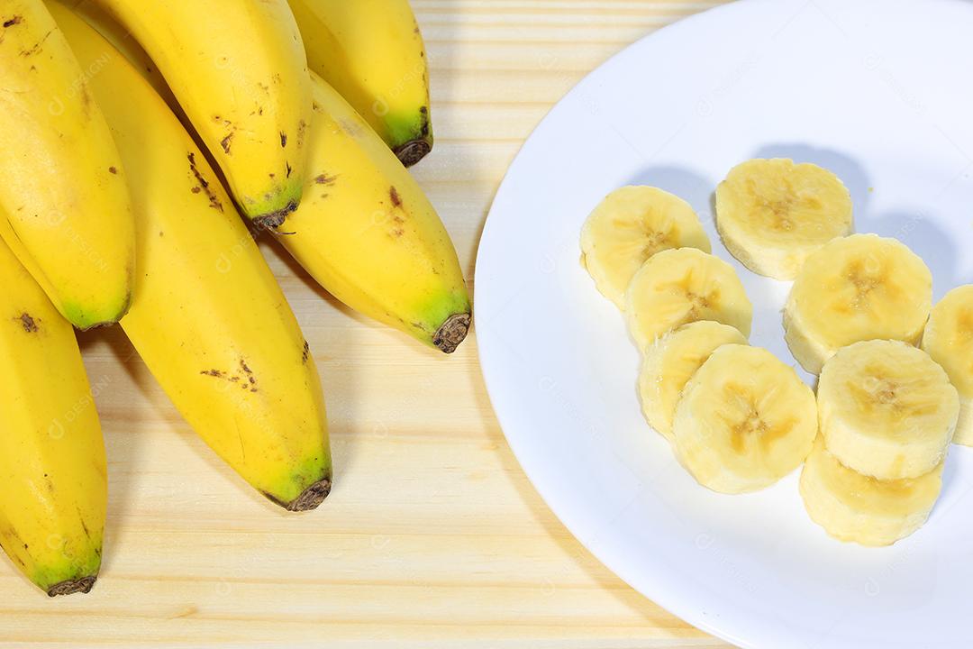 Bando de bananas na mesa de madeira ao lado do prato com frutas fatiadas