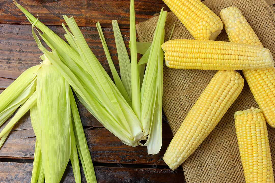 espiga de milho cru, com palha e casca, colhida da plantação, na mesa de madeira rústica. vista do topo