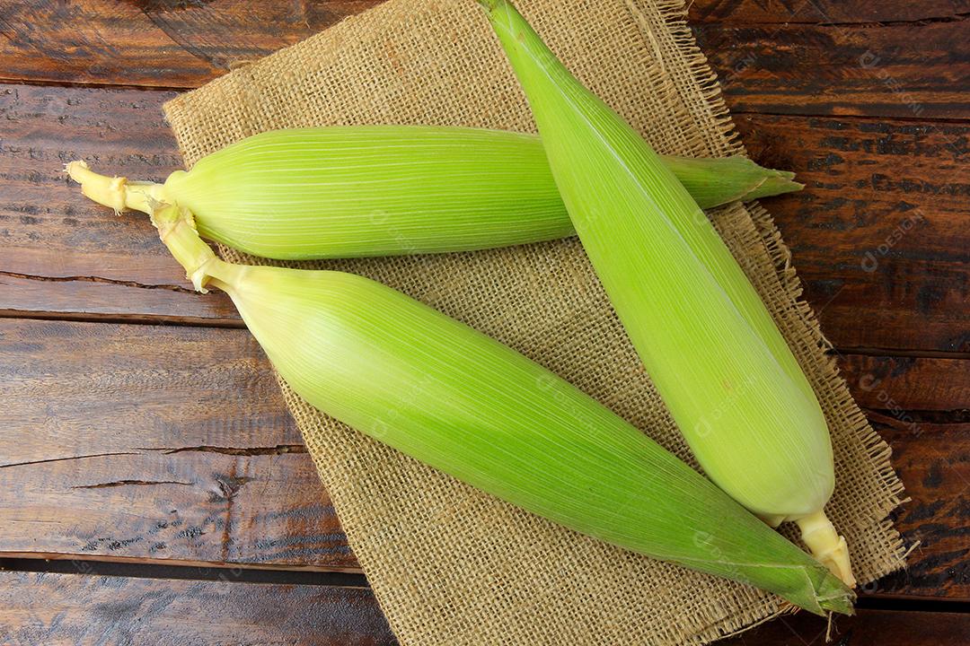 espiga de milho cru, com palha e casca, colhida da plantação, na mesa de madeira rústica. vista do topo