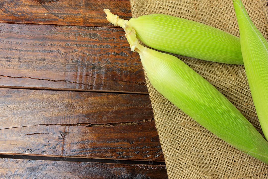 espiga de milho cru, com palha e casca, colhida da plantação, na mesa de madeira rústica. vista do topo