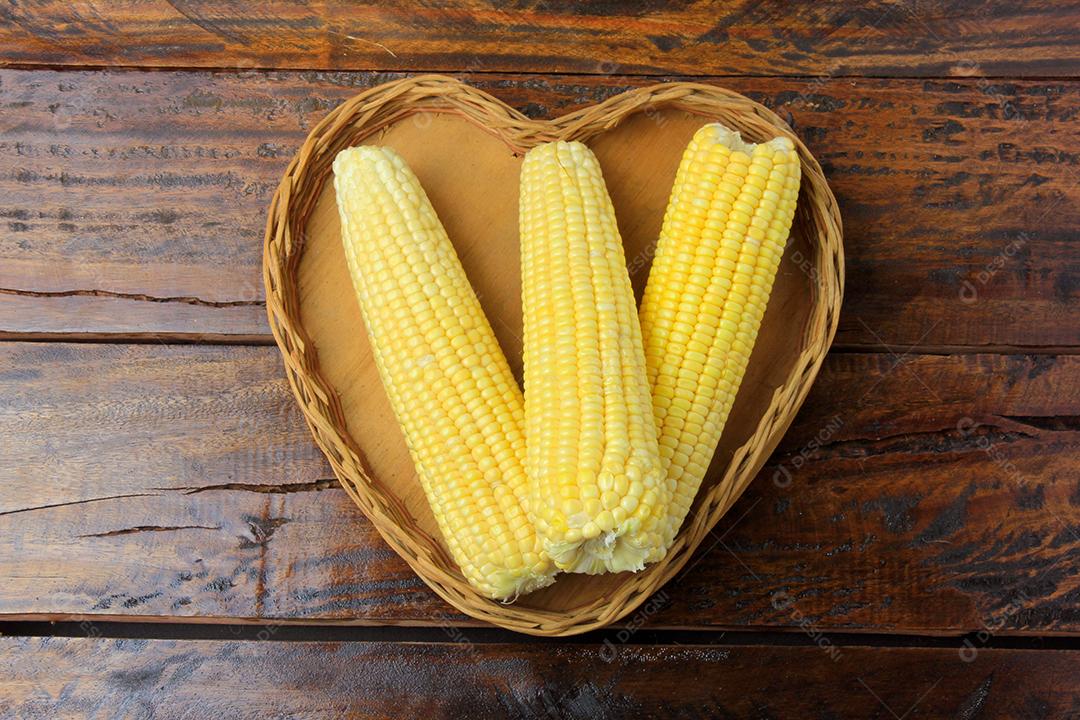 Corn on the cob, fresh, picked from the field inside the heart-shaped basket on the rustic wooden table