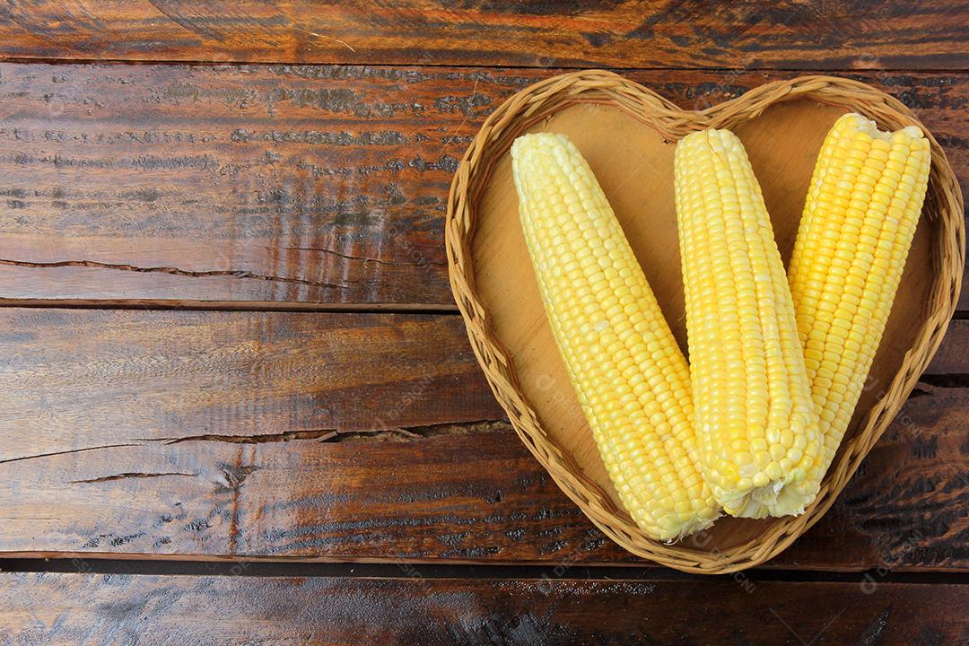 Espiga de milho, fresca, colhida da plantação dentro da cesta com forma de coração na mesa de madeira rústica