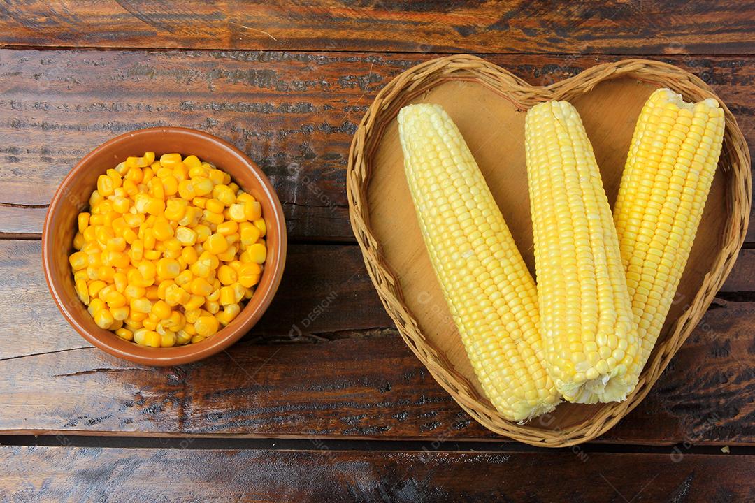 Espiga de milho, fresca, colhida da plantação dentro da cesta com forma de coração na mesa de madeira rústica