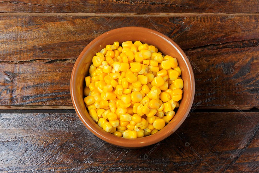 Grãos de milho cru dentro da tigela de cerâmica na mesa de madeira rústica