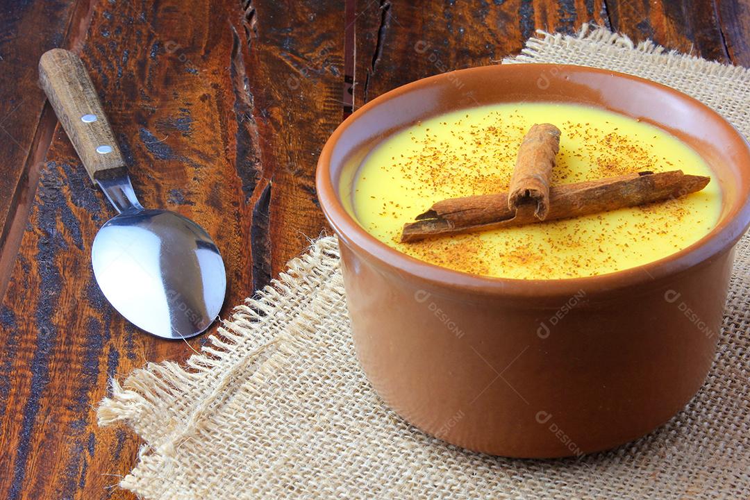 Curau, creme de milho doce e sobremesa típica da culinária brasileira, com canela colocada em tigela de cerâmica na mesa de madeira