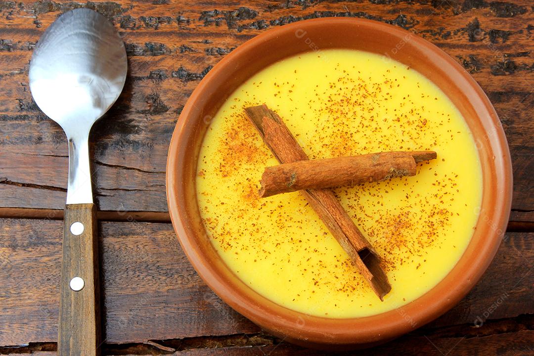 Curau, creme de milho doce e sobremesa típica da culinária brasileira, com canela colocada em tigela de cerâmica na mesa de madeira