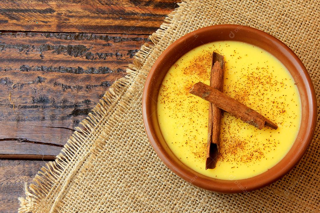 Curau, creme de milho doce e sobremesa típica da culinária brasileira, com canela colocada em tigela de cerâmica na mesa de madeira